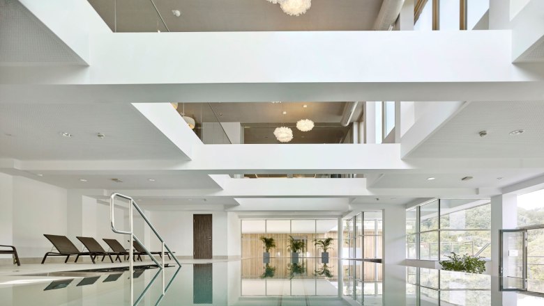 Indoorpool mit Liegestühlen und großen Fenstern.