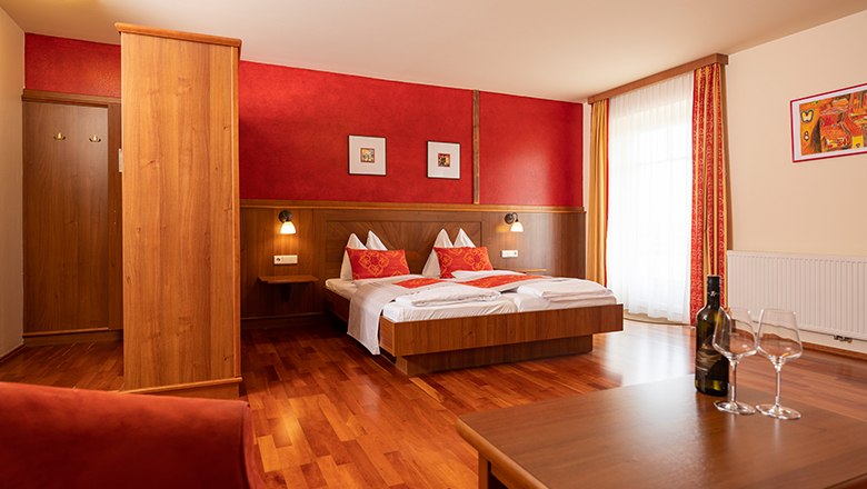 Gem&uuml;tliches Hotelzimmer mit Doppelbett, Holzm&ouml;beln und roten Akzenten.