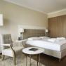 Modernes Hotelzimmer mit Doppelbett, Sessel, Tisch und Stehlampe.