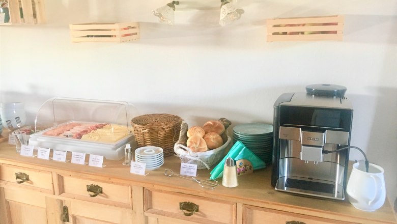 Frühstücksbuffet mit Aufschnitt, Brötchen und Kaffeemaschine auf einem Holztisch.