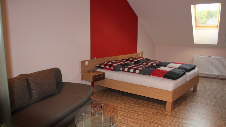 Modern eingerichtetes G&auml;stezimmer mit Bett, Sofa und Dachfenster.