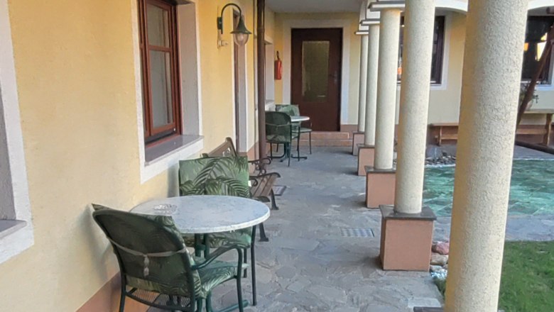 Ark&aacute;dov&eacute; n&aacute;dvoř&iacute; s kamennou podlahou, žlutou zd&iacute; a sloupy. Pod&eacute;l zdi jsou rozm&iacute;stěny stoly a židle.