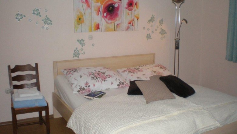 Gästezimmer, © Fam. Weinmann Ein gemütliches Gästezimmer mit einem Doppelbett, dekoriert mit floralen Kissen und einem Blumenbild an der Wand.