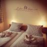 Cozy guest room with two beds, checkered comforters and pillows, decorative towels and a Goethe quote on the wall.
