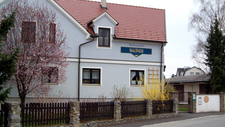 Ein zweistöckiges Haus mit rotem Dach und blauer Fassade, umgeben von blühenden Bäumen und einem Holzzaun.