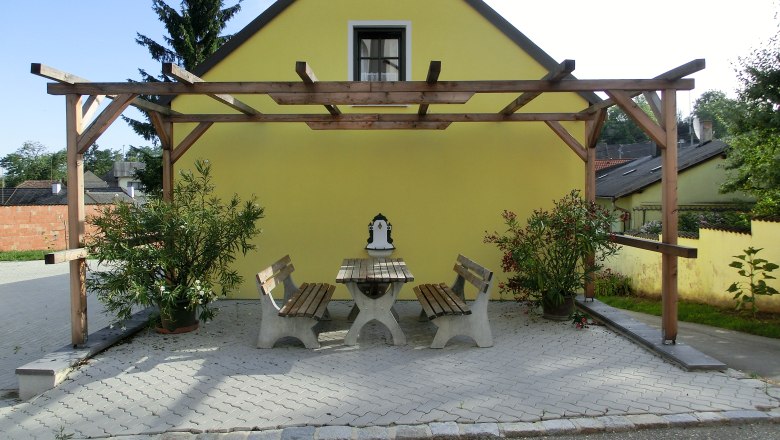 Gelbes Gebäude mit Pergola und Sitzbereich im Freien.