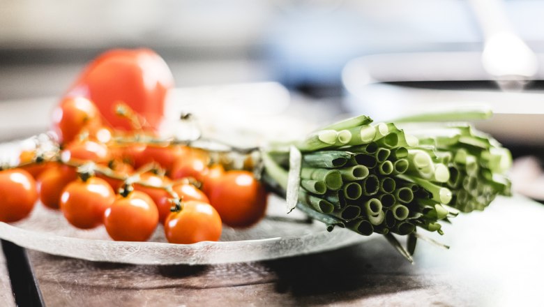Nahaufnahme von frischen Kirschtomaten und Fr&uuml;hlingszwiebeln auf einem Teller.