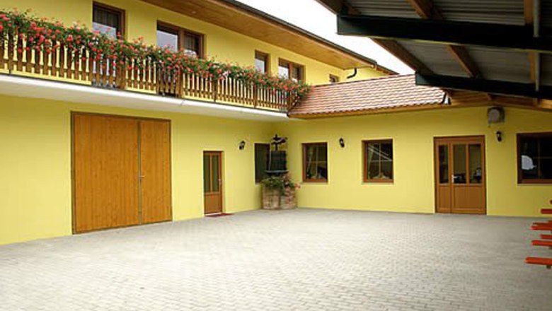 Innenhof eines gelben Gebäudes mit Holztüren und Balkon mit Blumen.