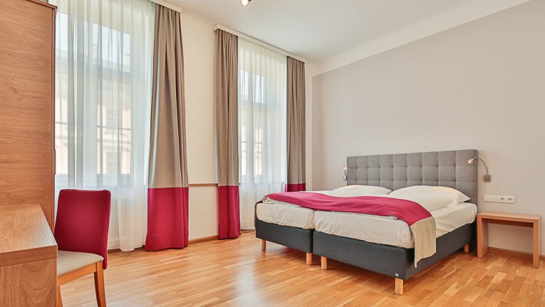Bright hotel room with double bed, desk and chair.