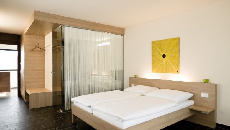 Modernes Hotelzimmer mit Doppelbett, Holzmöbeln und Glaswand.