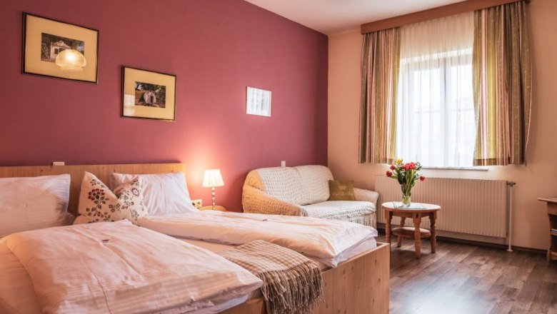 Gem&uuml;tliches G&auml;stezimmer mit Doppelbett, Sofa, Tisch und Blumenstrau&szlig;.