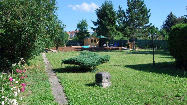 Garden with lawn, trees and a small path leading to a wooden house.