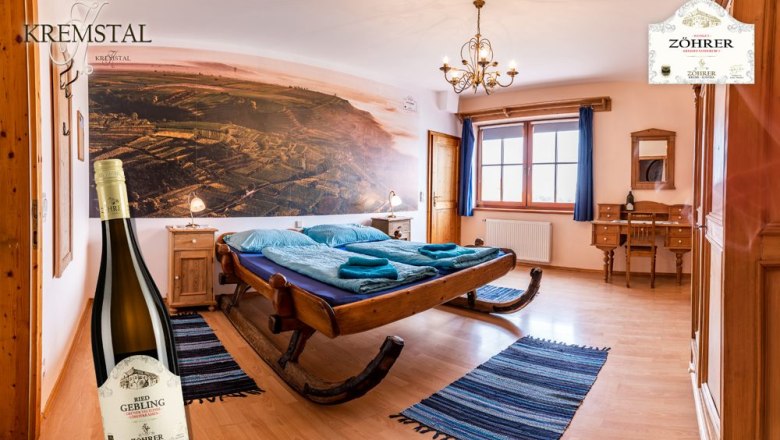 Cozy room with sleigh bed, wooden furniture and large mural. A bottle of wine stands in the foreground.