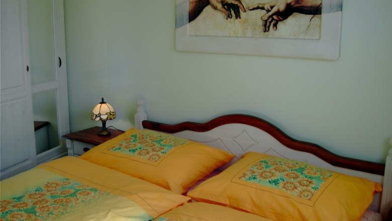 Pokoj pro hosty se žlut&yacute;m ložn&iacute;m pr&aacute;dlem, nočn&iacute; lampičkou a n&aacute;stěnnou malbou stvořen&iacute; Adama.