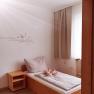 A simple guest room with a single bed, wooden shelf and a quote on the wall.