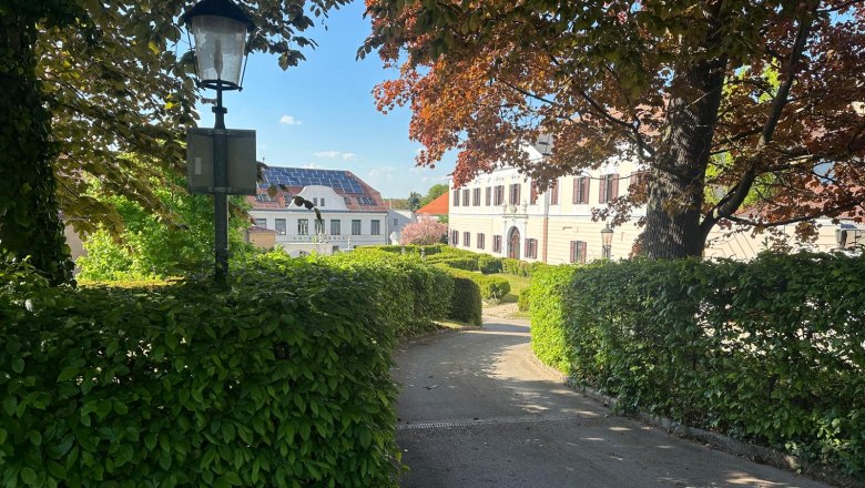 Pohled na z&aacute;mek v Gro&szlig;ru&szlig;bachu, obklopen&yacute; stromy a živ&yacute;m plotem, s lucernou v popřed&iacute;.