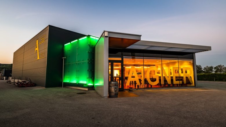 Modernes Weingut mit beleuchtetem Eingang und großem Schriftzug 'Aigner'.