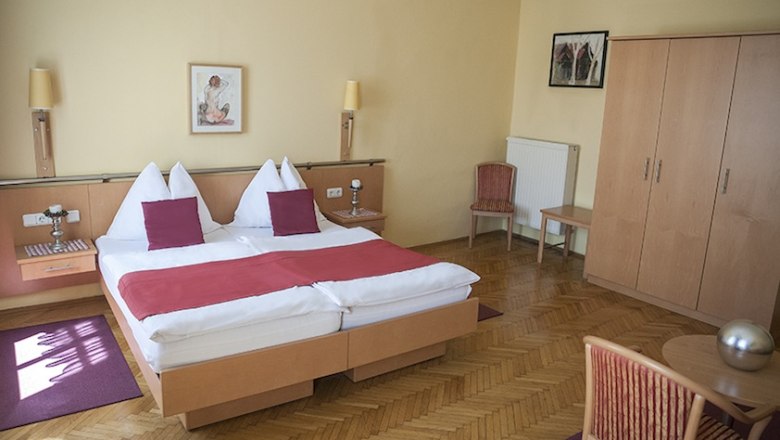 Hotelzimmer mit Doppelbett, Holzmöbeln und roten Akzenten.