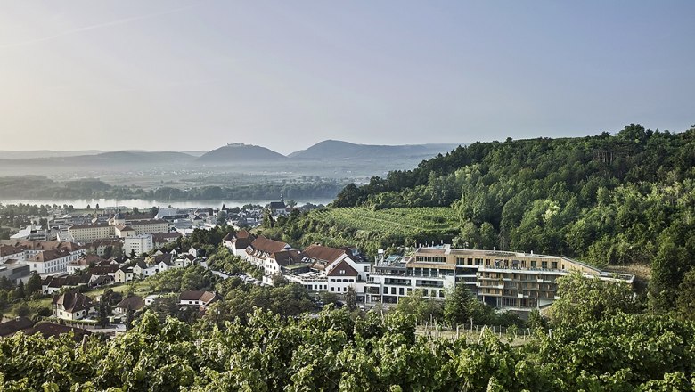 Blick auf das Steigenberger Hotel & Spa Krems umgeben von Weinbergen und Hügeln.