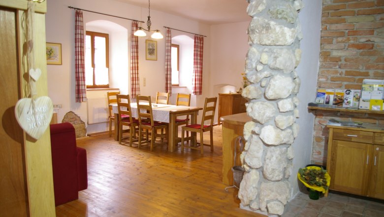 Gem&uuml;tlicher Essbereich mit Holztisch und St&uuml;hlen, roten Vorh&auml;ngen und Steinmauer.