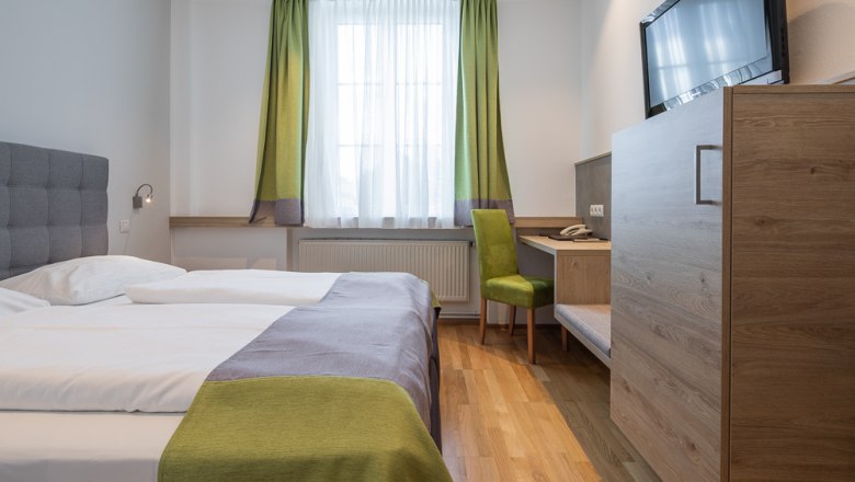 Modernes Hotelzimmer mit Doppelbett, Schreibtisch und Fernseher.