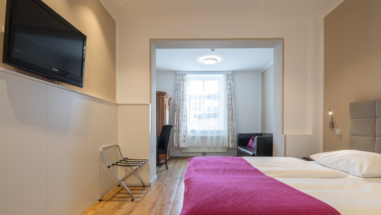 Hotelzimmer mit Doppelbett, Fernseher und Sitzbereich.
