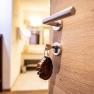 Detailn&iacute; z&aacute;běr dřevěn&yacute;ch dveř&iacute; s kl&iacute;čem v z&aacute;mku a dřevěn&yacute;m př&iacute;věskem. V pozad&iacute; je rozmazan&aacute; světl&aacute; m&iacute;stnost.