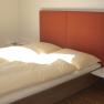 Modernes Gästezimmer mit Doppelbett, rotem Kopfteil und Pflanzen.