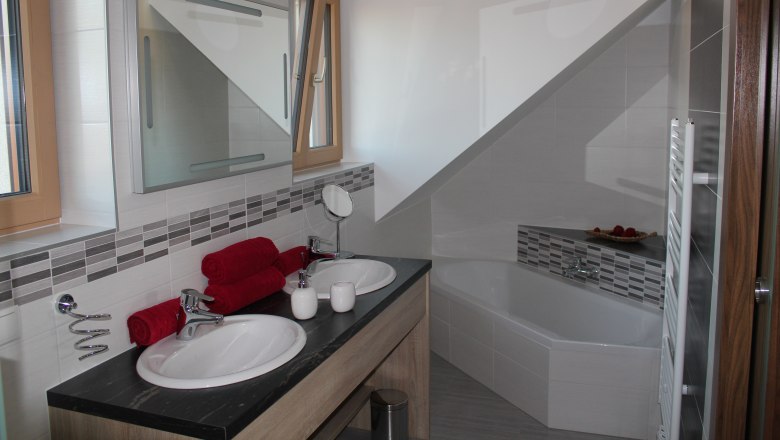 Modern bathroom with double washbasin, bathtub and red towels.