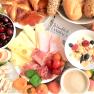 Ein reichhaltiges Frühstück mit Käse, Schinken, Croissants, Obst, Müsli, Ei und Kaffee auf einem Tisch.