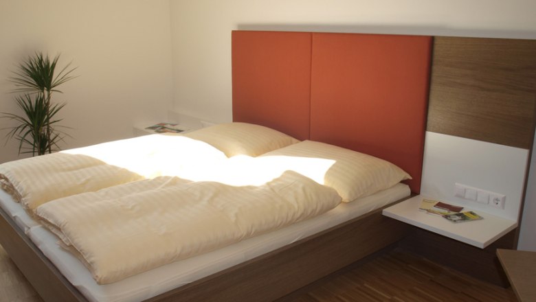 Modernes G&auml;stezimmer mit Doppelbett, rotem Kopfteil und Pflanzen.