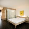 Modernes Hotelzimmer mit Doppelbett, Holzm&ouml;beln und Glaswand.