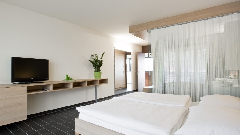 Modernes Hotelzimmer mit Doppelbett, Fernseher und Pflanzen.