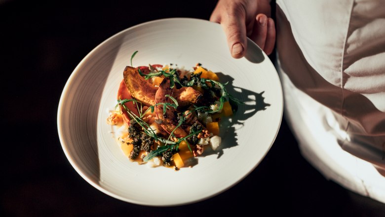 Ein Teller mit einem kunstvoll angerichteten Gericht, gehalten von einer Person in wei&szlig;er Kleidung.