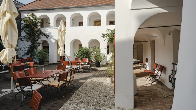 Innenhof mit weißen Arkaden, Holzmöbeln und Sonnenschirmen.