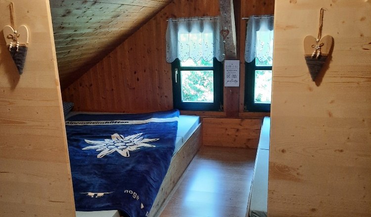 &Uacute;tuln&aacute; ložnice s matracemi v podkrov&iacute; s dřevěn&yacute;m obložen&iacute;m a dvěma okny.