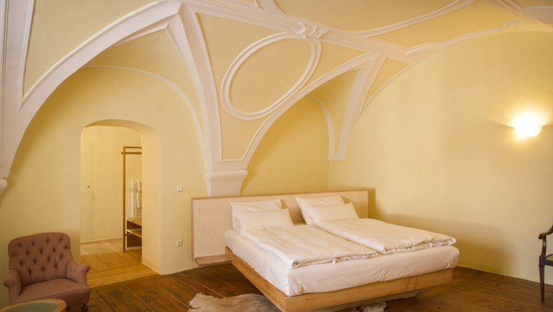 Oberstockstall Estate, © Robert Herbst An elegant bedroom with a vaulted ceiling, a double bed, an armchair and wooden floor.