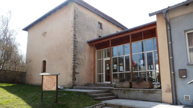 Historick&aacute; budova s modern&iacute; př&iacute;stavbou a n&aacute;pisem v popřed&iacute;.