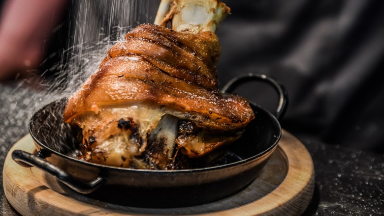 Křupav&eacute; vepřov&eacute; koleno na p&aacute;nvi na dřevěn&eacute;m prk&eacute;nku, posypan&eacute; sol&iacute;.