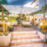 Cozy guest garden with tables, chairs and parasols, surrounded by plants and lights.