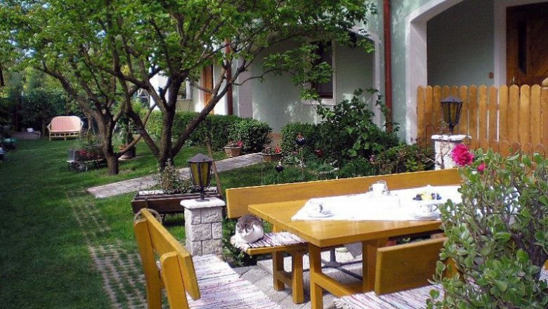 Ein gepflegter Garten mit Holzm&ouml;beln, einer Katze auf der Bank und einem gedeckten Tisch.