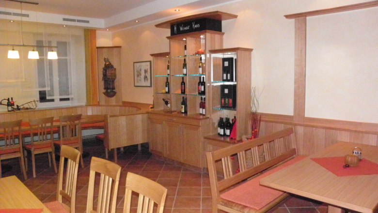 Innenansicht eines gemütlichen Gastraums mit Holzmöbeln und Weinregal.