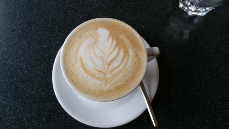 Eine Tasse Cappuccino mit Latte Art in Form eines Blattes auf einem dunklen Tisch.