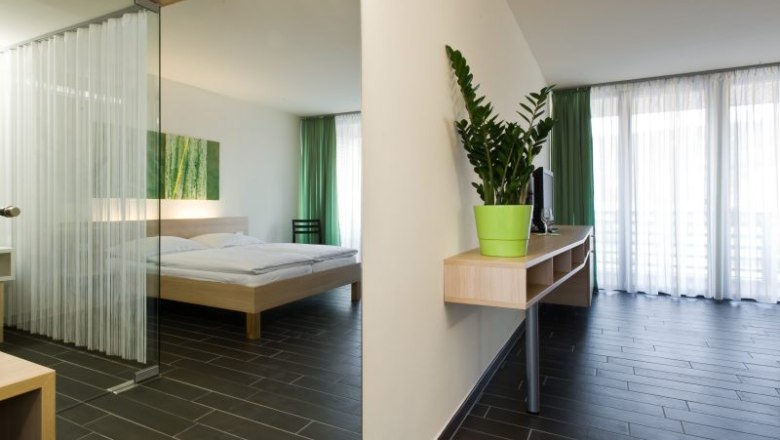 Modernes Hotelzimmer mit Doppelbett, grünem Vorhang und Zimmerpflanze.