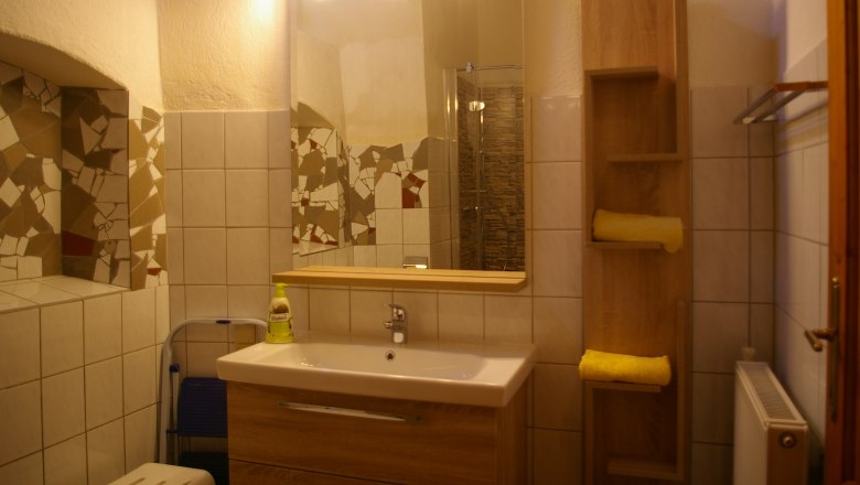Badezimmer mit Spiegel, Waschbecken, Fliesen und Regal mit Handt&uuml;chern.