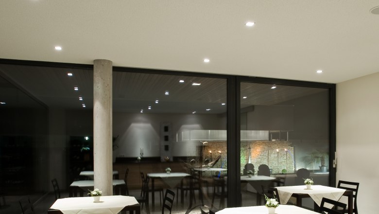 Moderner Frühstücksraum mit Tischen und Stühlen, dekoriert mit weißen Tischdecken und Blumen.