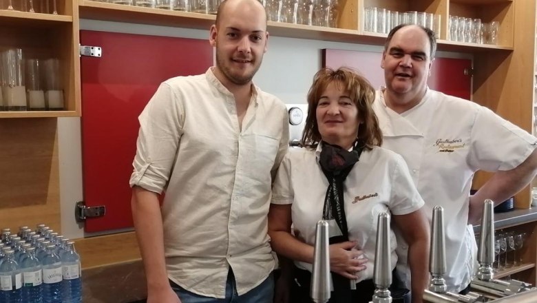 Tři lid&eacute; stoj&iacute; za barem s v&yacute;čepn&iacute;mi zař&iacute;zen&iacute;mi a sklenicemi v pozad&iacute;.