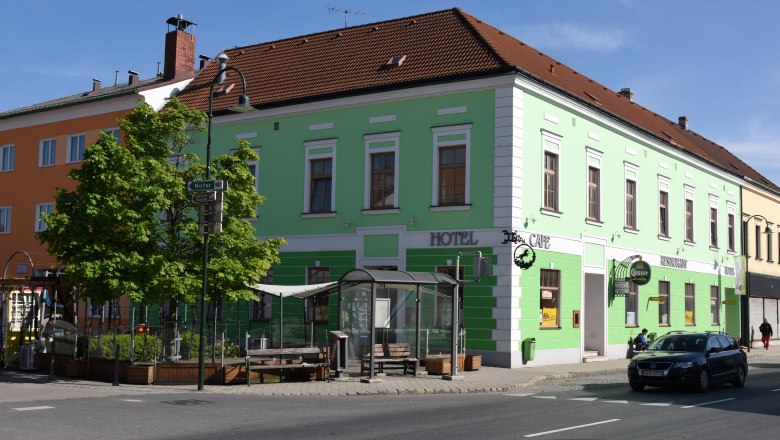 Green building with hotel and caf&eacute; signs on a street corner.