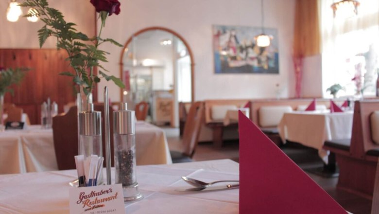 Pohled do interi&eacute;ru &uacute;tuln&eacute; restaurace s prostřen&yacute;mi stoly, červen&yacute;mi ubrousky a růž&iacute; ve v&aacute;ze.