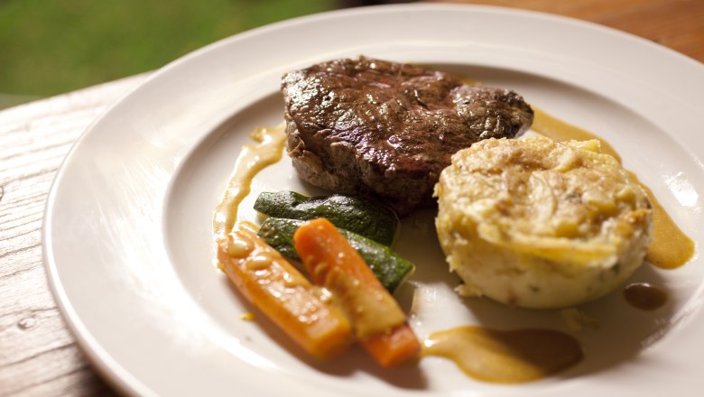 Ein Teller mit einem St&uuml;ck Fleisch, Gem&uuml;se und einer Kartoffelbeilage.
